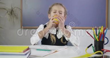 迷人的白人女学生在练习本上写字，咬着苹果，伸出大拇指。快乐女生做